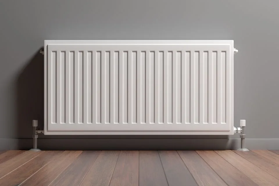 Witte paneelradiator tegen een grijze muur boven een houten vloer
